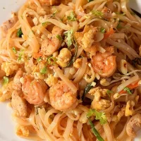 a white plate with authentic pad thai recipe with crushed peanuts ,beans,chicken and shrimp